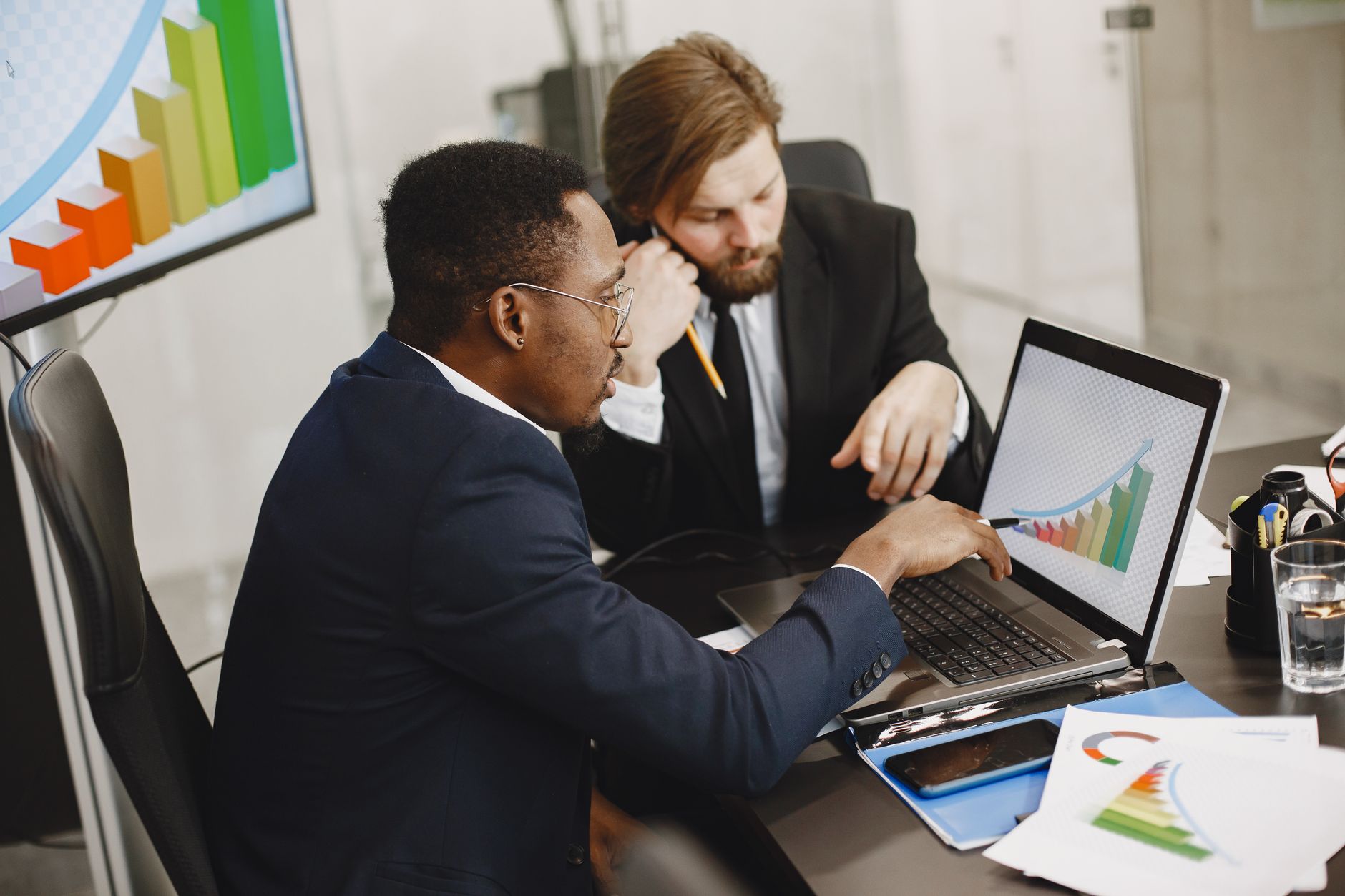 Two business professionals working on growth charts using laptop in an office setting. — BrightFinance - Trade a Variety of A
