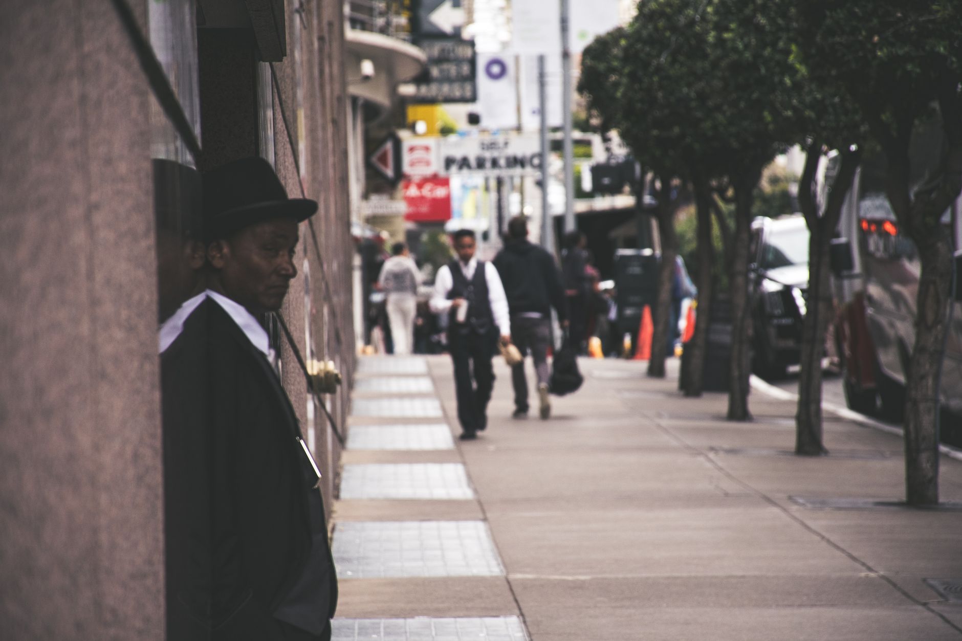 A man in a suit and hat leans against a city building, observing pedestrians. — How Can My ISO Offer Cash Discount Merchant S