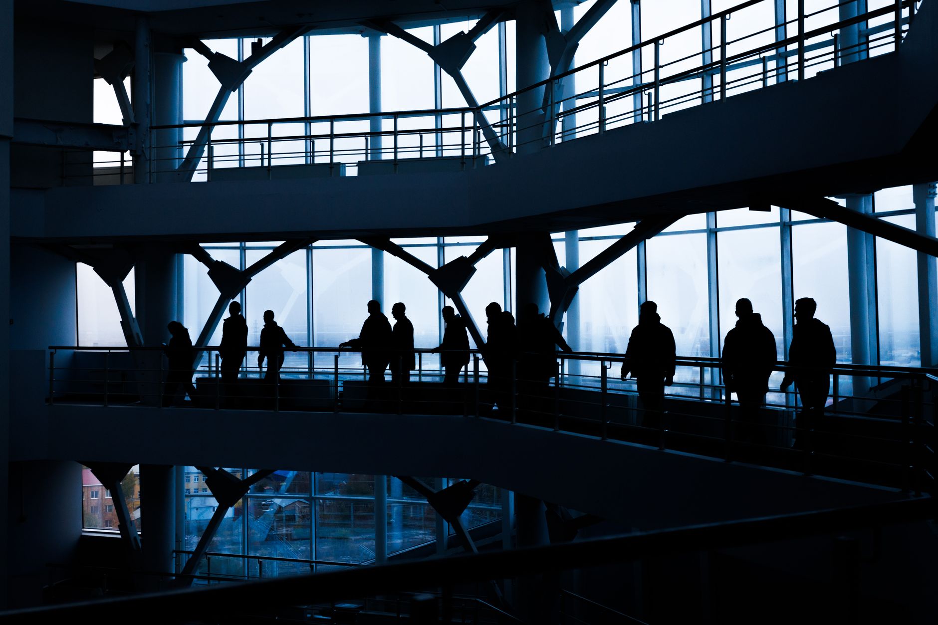 Silhouettes of people walking in a modern architectural building with large windows. — How does Covid-19 impact income protec