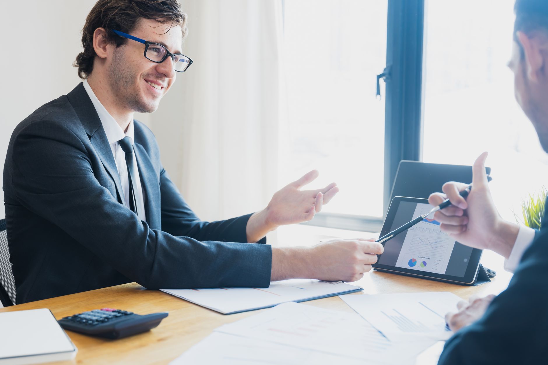 Two businessmen in formal attire discussing a business report in an office setting with a tablet. — Reasons Why Social Media