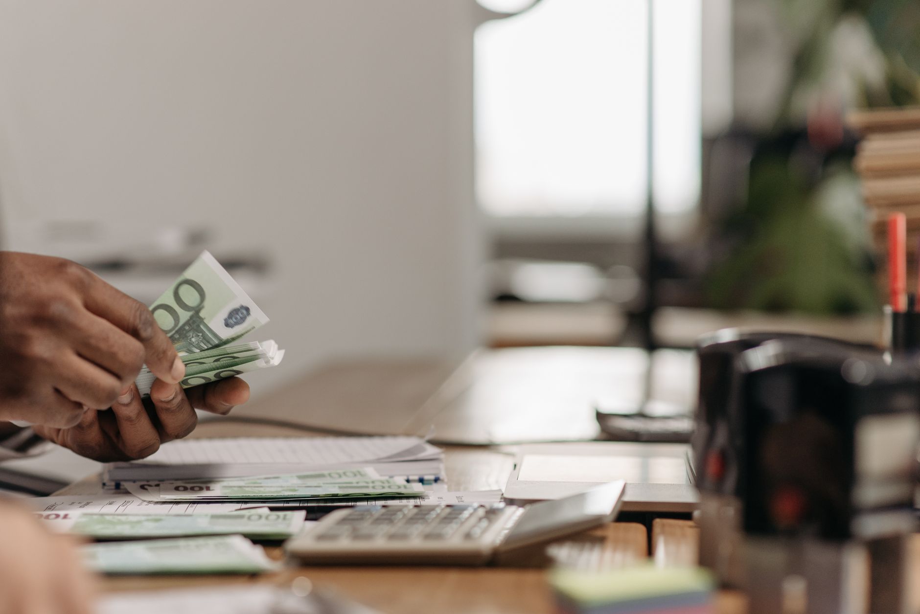 Close-up of hands counting euro bills at an office desk with a calculator. — Secure Your Investments with a Demat Acc