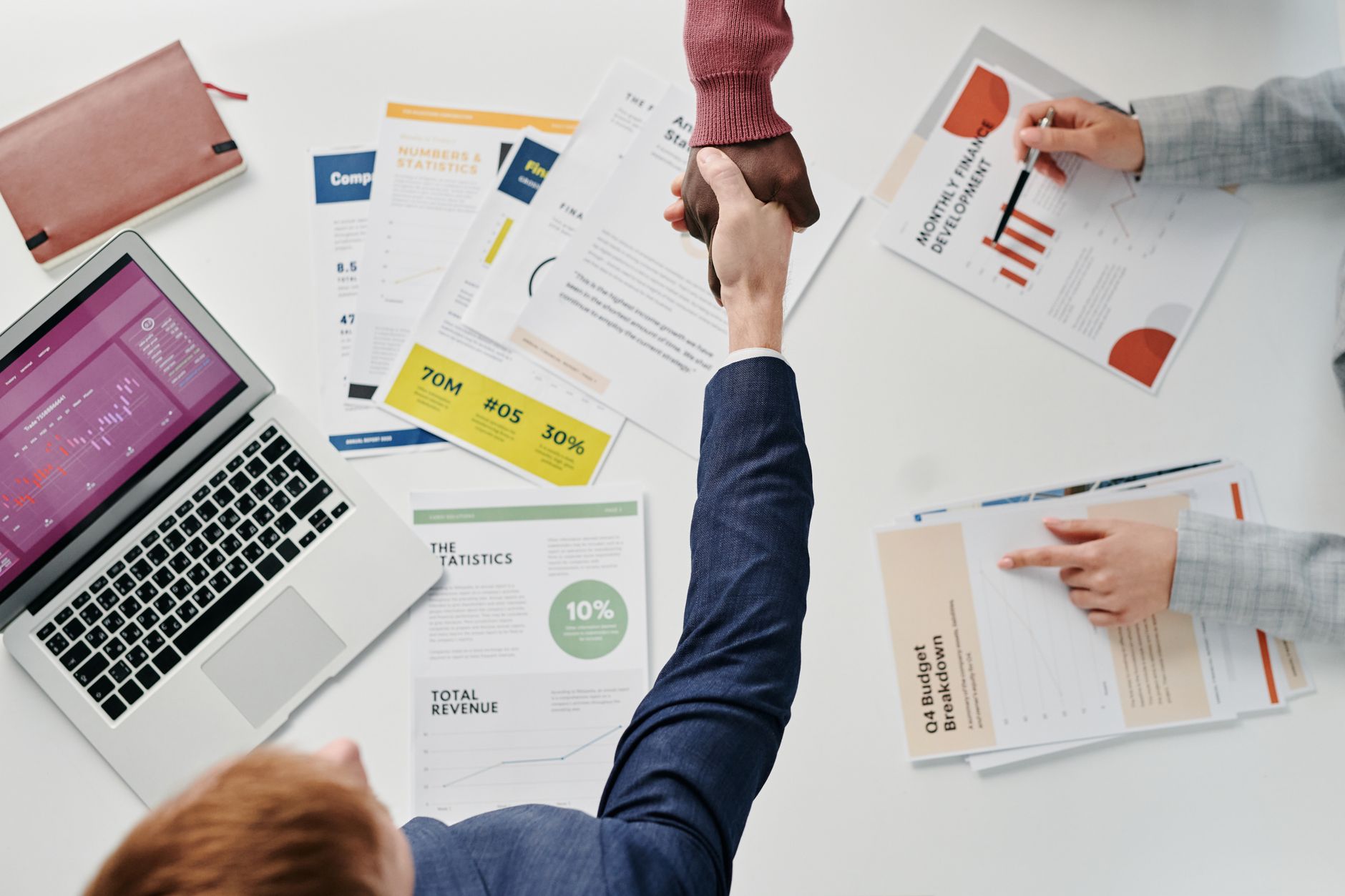 Business professionals engaging in a handshake over a desk filled with financial documents and a laptop. — The Role of HCG in