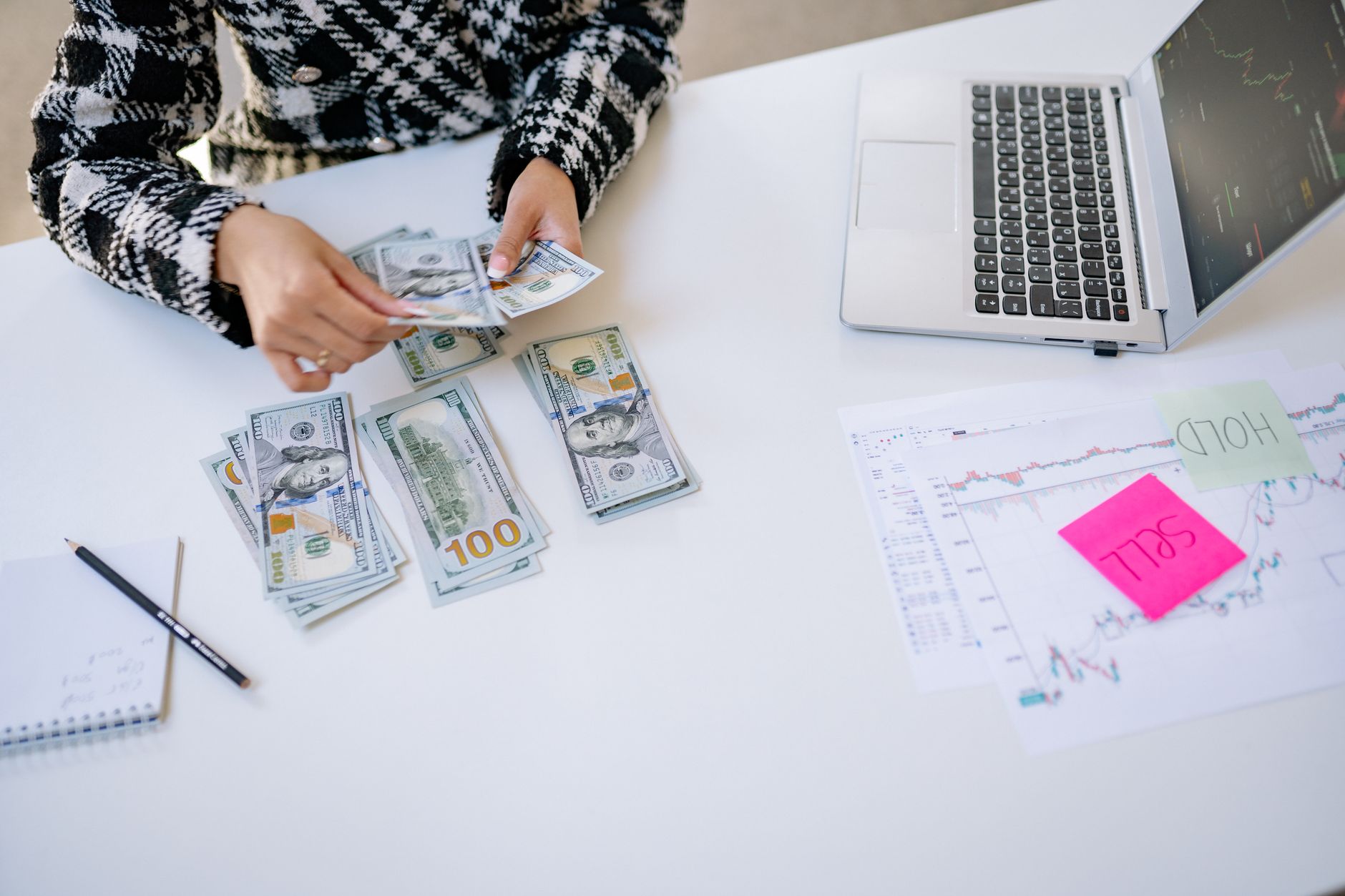 Person counting cash next to laptop and stock market charts on a white table. — Use the comparative market analysis for the t